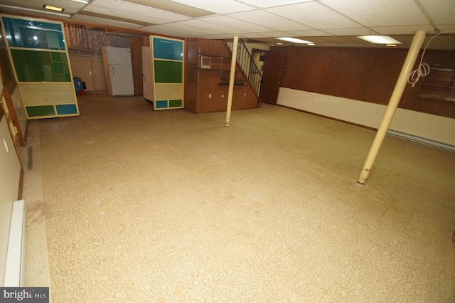 finished basement featuring wooden walls, stairway, freestanding refrigerator, and a paneled ceiling