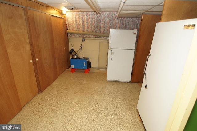 finished basement featuring a drop ceiling, wallpapered walls, and freestanding refrigerator