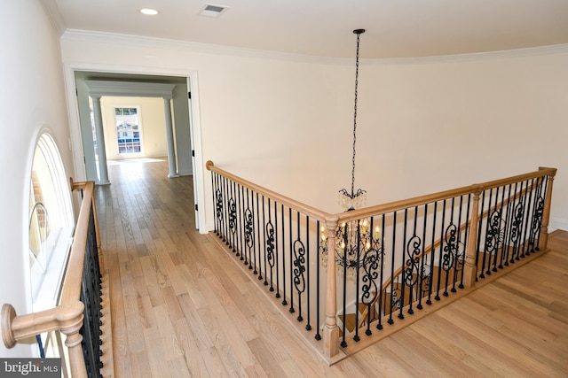 hallway with a notable chandelier, wood finished floors, an upstairs landing, visible vents, and ornamental molding