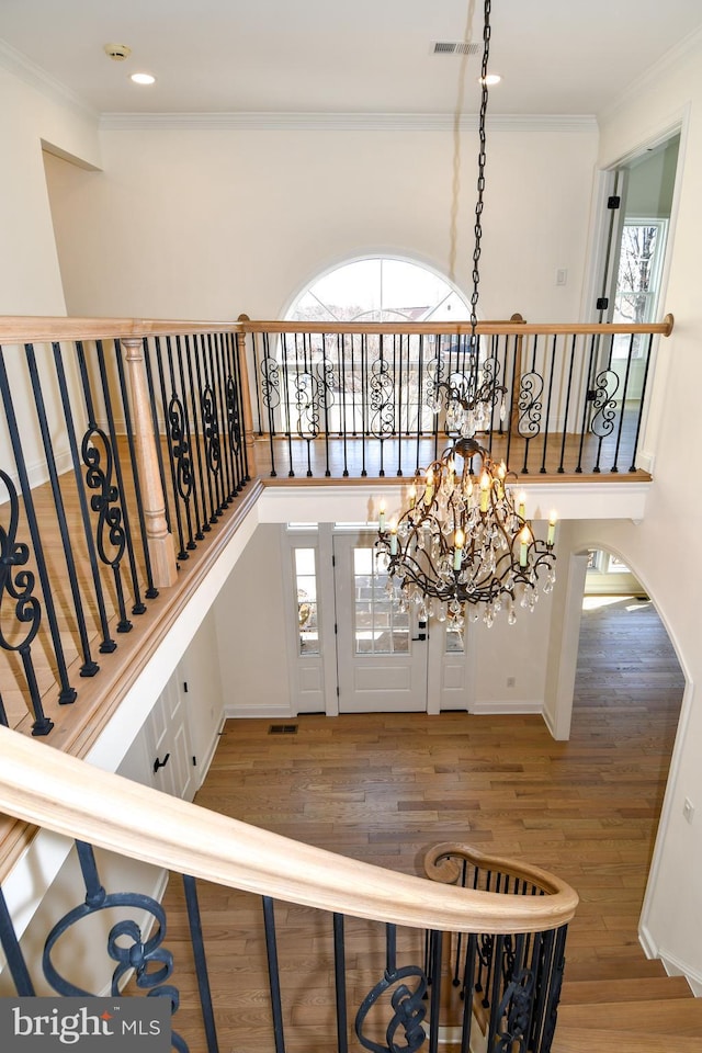 staircase featuring a chandelier, wood finished floors, visible vents, and crown molding