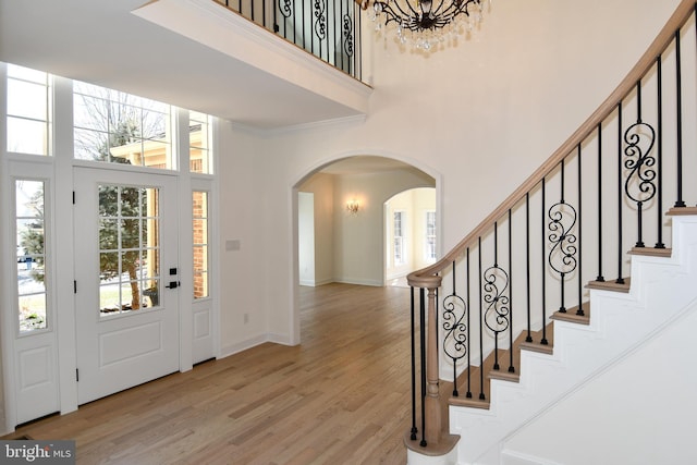 foyer with arched walkways, a high ceiling, light wood-type flooring, and stairs