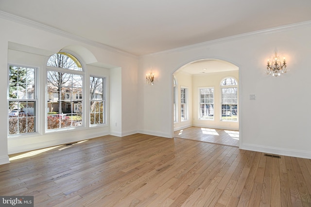 spare room featuring arched walkways, ornamental molding, light wood-type flooring, and visible vents