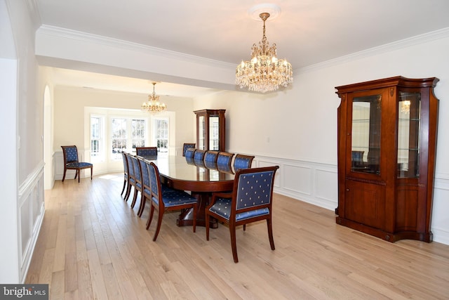 dining area with a wainscoted wall, a notable chandelier, light wood finished floors, a decorative wall, and ornamental molding