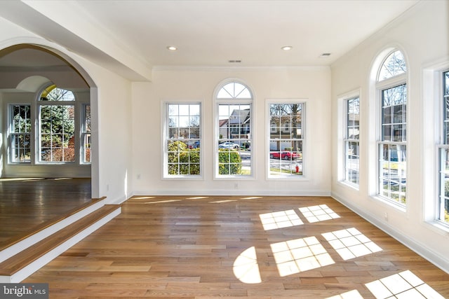 unfurnished sunroom featuring a wealth of natural light, visible vents, and arched walkways