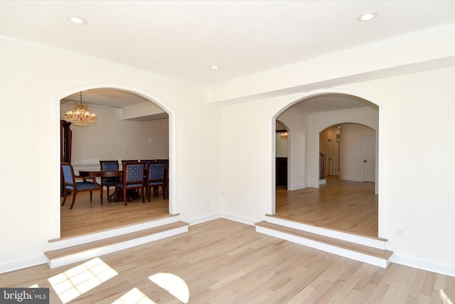 empty room featuring arched walkways, light wood-type flooring, a chandelier, and recessed lighting