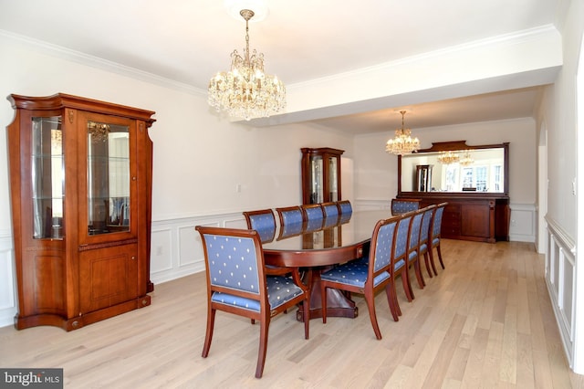 dining space featuring crown molding, light wood-style floors, wainscoting, and a notable chandelier