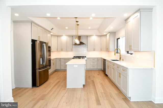 kitchen featuring stainless steel appliances, a kitchen island, a sink, wall chimney range hood, and a raised ceiling