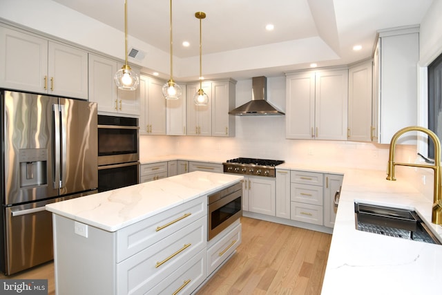 kitchen with light stone counters, light wood finished floors, stainless steel appliances, a sink, and wall chimney range hood