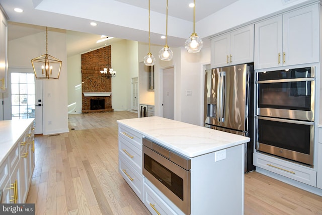 kitchen with stainless steel appliances, lofted ceiling, a brick fireplace, and light wood finished floors