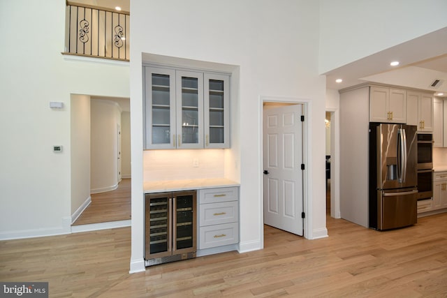 kitchen with double oven, wine cooler, light wood finished floors, and stainless steel fridge with ice dispenser