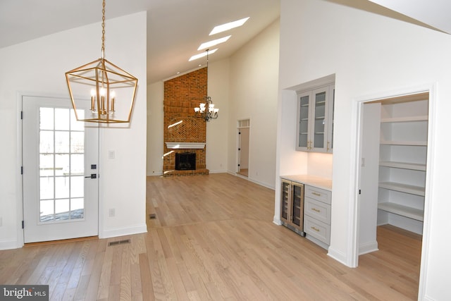 interior space featuring a chandelier, high vaulted ceiling, light wood-style flooring, beverage cooler, and a fireplace