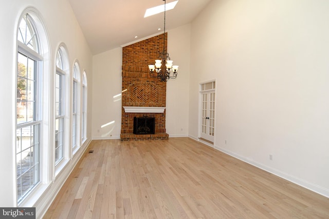 unfurnished living room with high vaulted ceiling, a notable chandelier, baseboards, light wood-style floors, and a brick fireplace