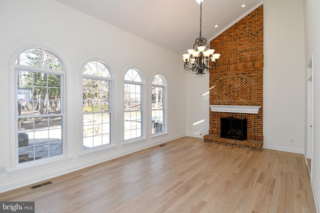 unfurnished living room with visible vents, light wood-style flooring, an inviting chandelier, a brick fireplace, and high vaulted ceiling