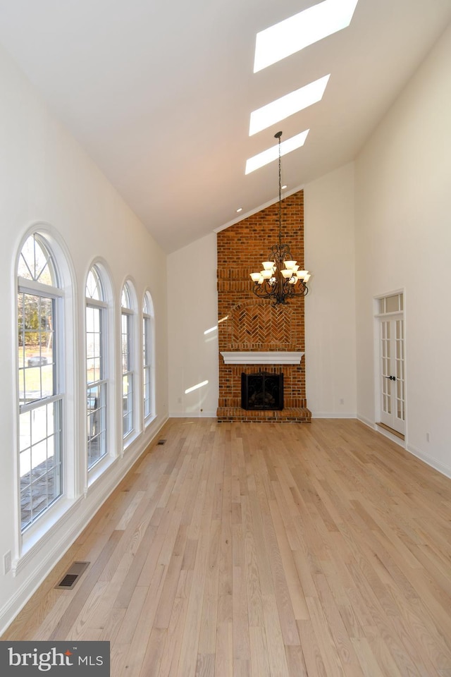 unfurnished living room with light wood finished floors, visible vents, a fireplace, high vaulted ceiling, and a notable chandelier