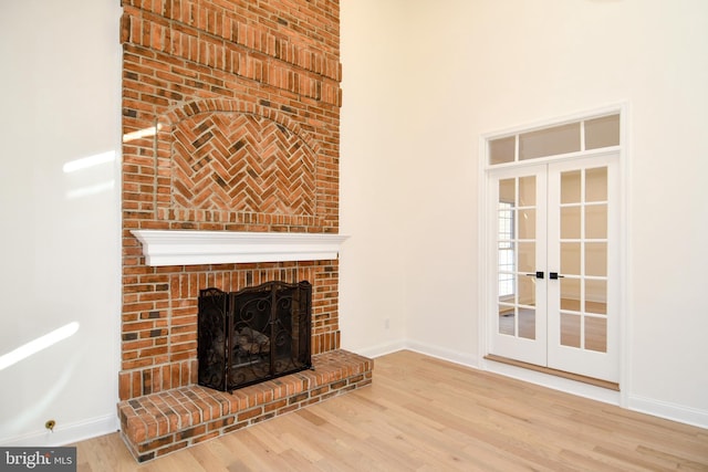 unfurnished living room featuring french doors, a fireplace, a high ceiling, wood finished floors, and baseboards