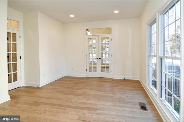 unfurnished room featuring a healthy amount of sunlight, light wood-style floors, visible vents, and french doors