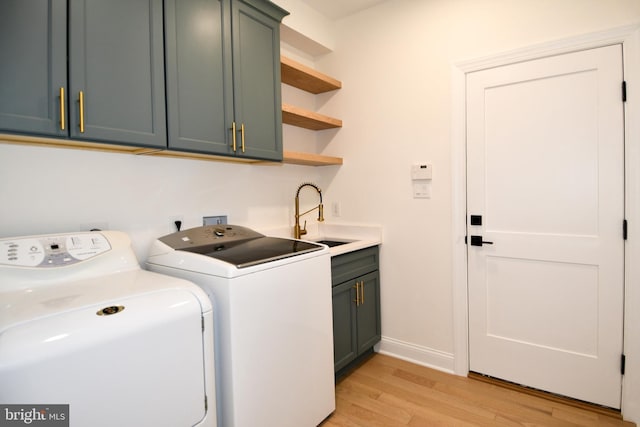 laundry area with a sink, baseboards, cabinet space, light wood finished floors, and washer and clothes dryer