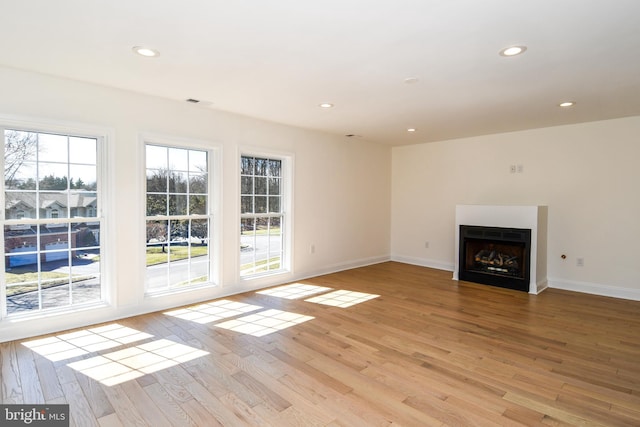 unfurnished living room with light wood-type flooring, a fireplace, baseboards, and recessed lighting