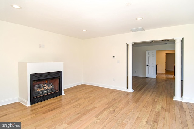 unfurnished living room with light wood-style floors, baseboards, a fireplace, and ornate columns