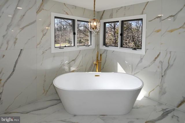 full bathroom featuring a chandelier, a freestanding tub, marble finish floor, and stone wall