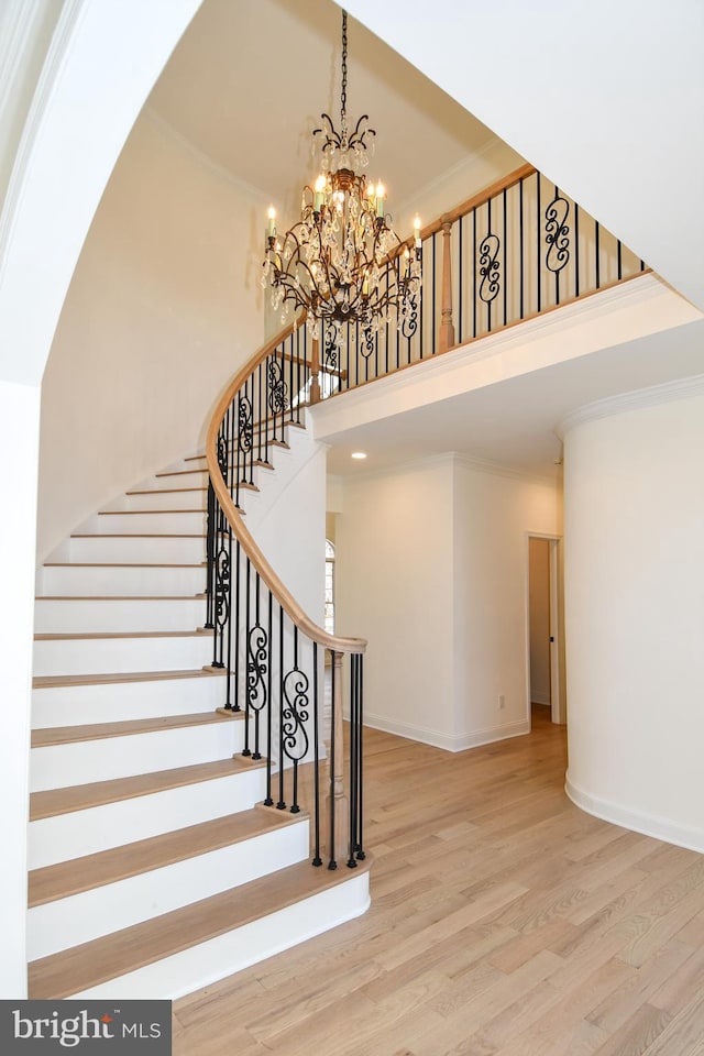 staircase with baseboards, ornamental molding, wood finished floors, an inviting chandelier, and a high ceiling