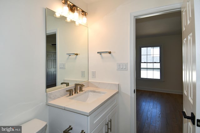 half bath featuring baseboards, vanity, toilet, and wood finished floors