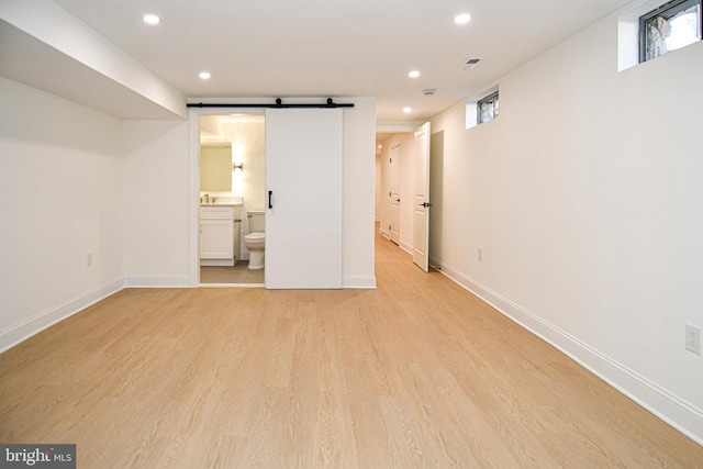 basement featuring plenty of natural light, a barn door, light wood-type flooring, and recessed lighting