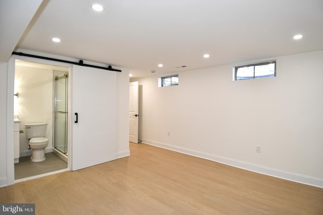 basement with a barn door, light wood-type flooring, a wealth of natural light, and recessed lighting