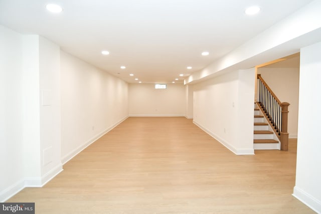 finished below grade area featuring light wood finished floors, stairway, baseboards, and recessed lighting