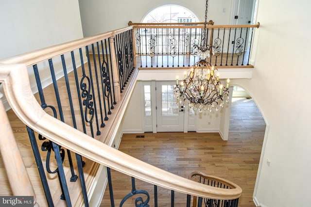 stairs with wood finished floors, a towering ceiling, baseboards, and an inviting chandelier