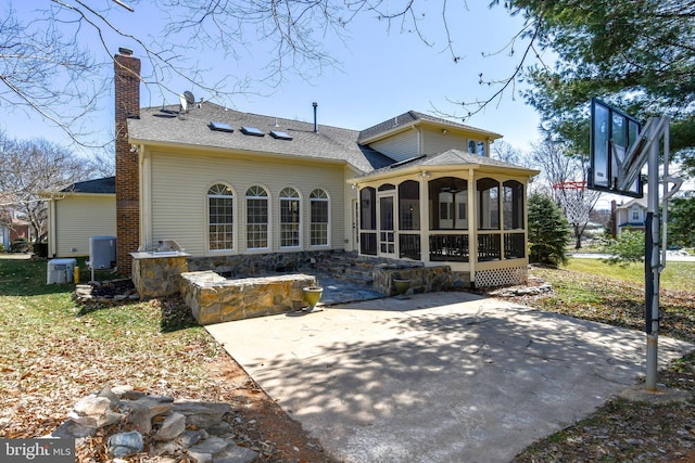 rear view of property with a patio, a chimney, a shingled roof, central AC unit, and a sunroom