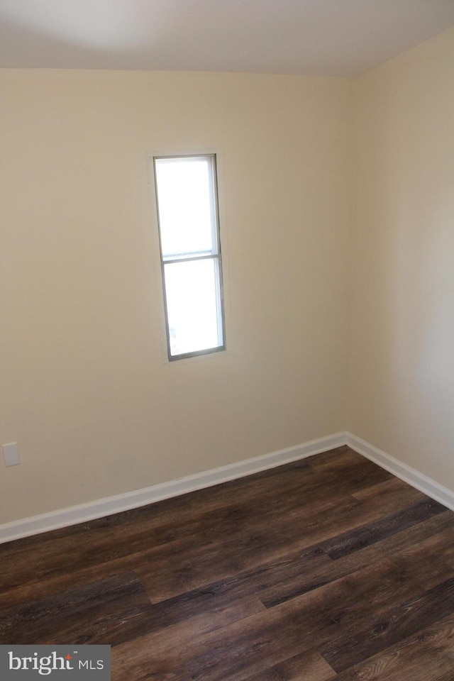 spare room featuring baseboards and dark wood-style flooring