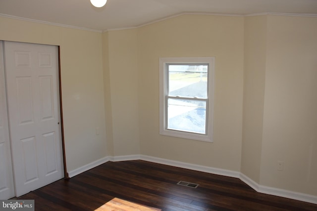 spare room with crown molding, dark wood-style flooring, visible vents, and baseboards