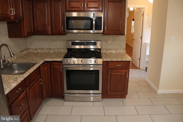 kitchen featuring light tile patterned floors, tasteful backsplash, baseboards, stainless steel appliances, and a sink