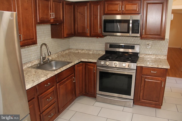 kitchen featuring appliances with stainless steel finishes, a sink, backsplash, and light stone countertops