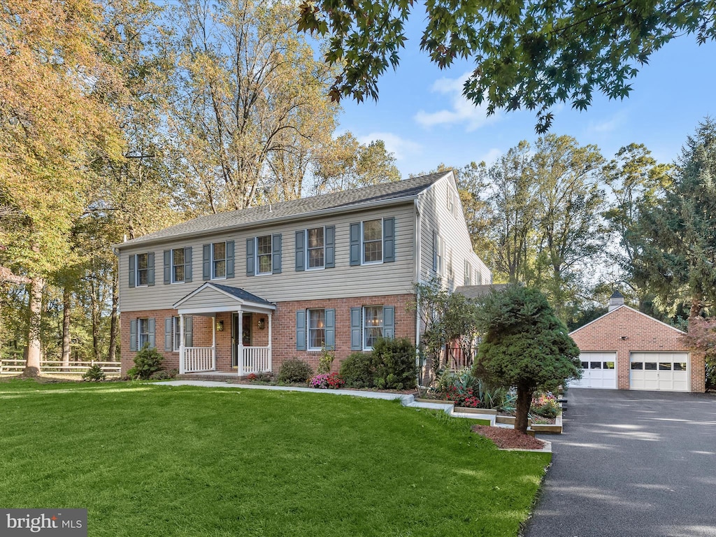 view of front of property with brick siding, a detached garage, a front lawn, and fence