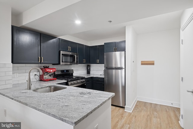 kitchen with light stone counters, a sink, stainless steel appliances, light wood-style floors, and backsplash