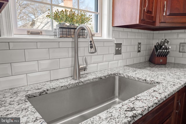 room details featuring a sink, decorative backsplash, and light stone countertops