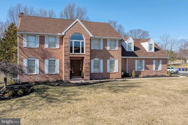 view of front of home featuring brick siding, a front lawn, and a shingled roof