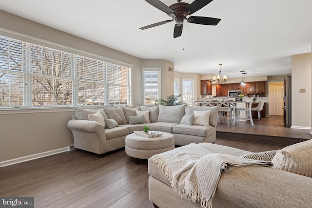 living room featuring ceiling fan with notable chandelier, baseboards, and wood finished floors