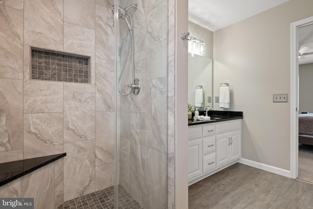 bathroom featuring baseboards, a tile shower, ensuite bathroom, wood finished floors, and vanity