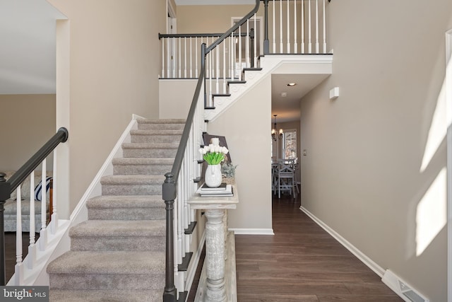 stairway featuring visible vents, wood finished floors, an inviting chandelier, baseboards, and a towering ceiling