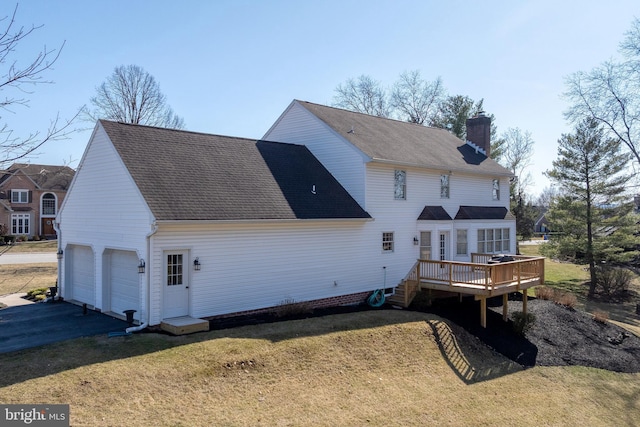 rear view of property featuring roof with shingles, a yard, a chimney, a garage, and a deck