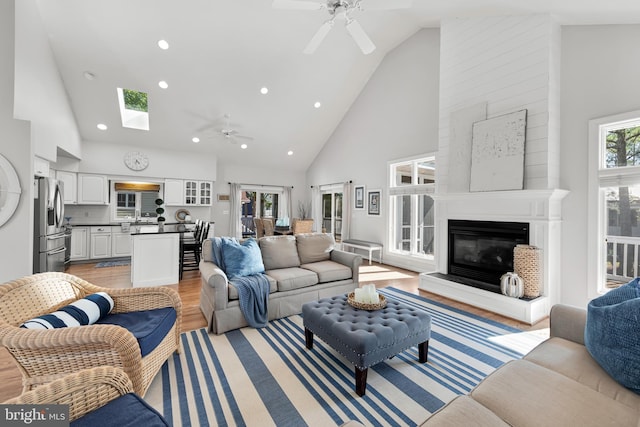 living area with high vaulted ceiling, a large fireplace, light wood-style flooring, and a ceiling fan