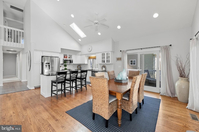 dining area featuring high vaulted ceiling, visible vents, a skylight, light wood finished floors, and ceiling fan