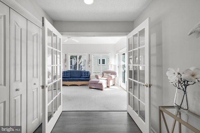 hall with dark wood finished floors, french doors, and a textured ceiling