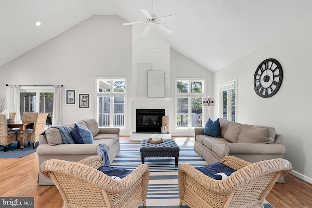 living area with high vaulted ceiling, a large fireplace, baseboards, and wood finished floors