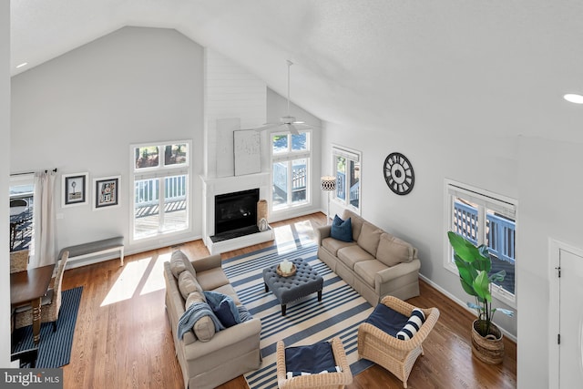 living area with high vaulted ceiling, a fireplace, wood finished floors, a ceiling fan, and baseboards