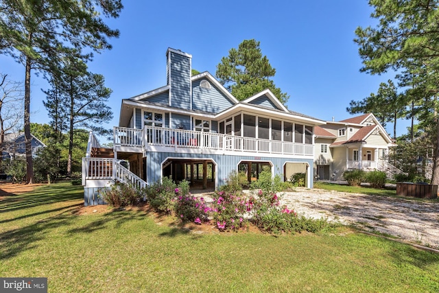 rear view of house with a sunroom, stairway, a lawn, driveway, and a chimney
