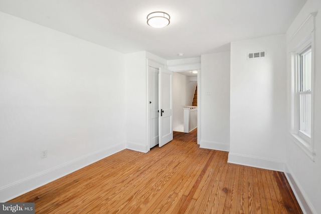 unfurnished room with stairs, light wood-type flooring, visible vents, and baseboards